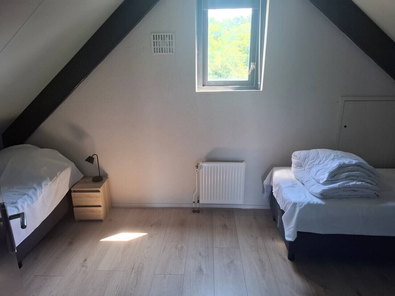 A room with two beds, a radiator, a window, and a small table.