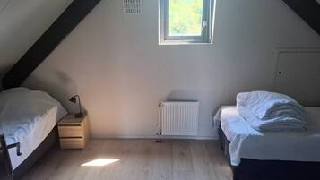 A room with two beds, a radiator, a window, and a small table.