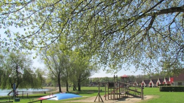 Un parco con un'area giochi, una zona giochi blu e una distesa d'acqua sullo sfondo.