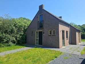 A single-story brick house with a front door, a small balcony, and a paved driveway. - Vakantiehuis op vakantiepark `t Broeckhuys. (Ewijk)