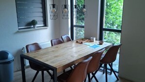 Un'area pranzo moderna con un tavolo di legno, sei sedie, lampade a sospensione e ampie finestre vista su un'area verde.