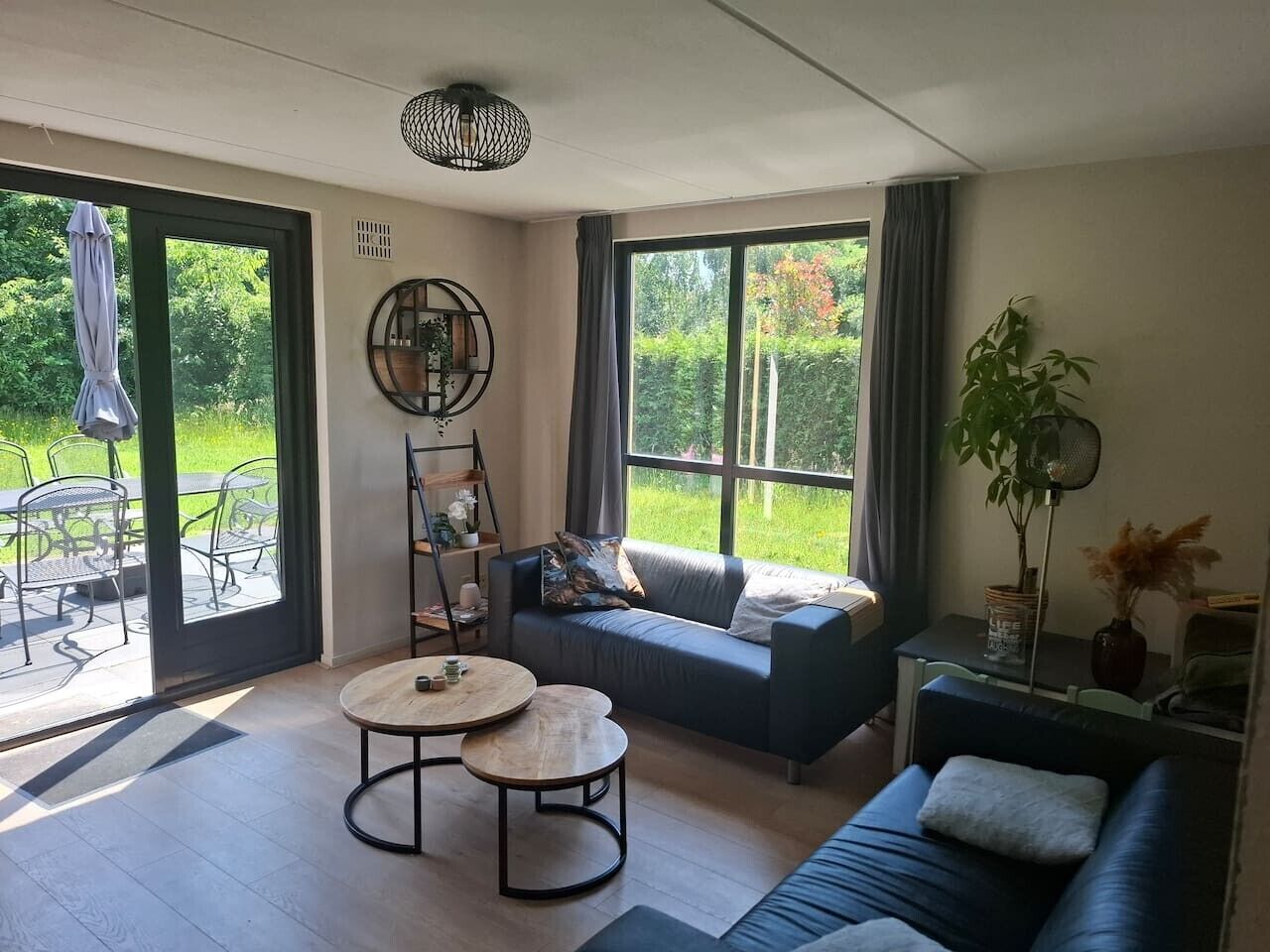 Ein modernes Wohnzimmer mit einer Couch, zwei runden Tischen und einem großen Fenster mit Blick ins Freie.