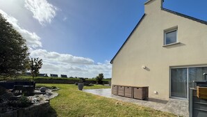A modern building with a flat roof, a large window, and a paved patio area. - Charming house near the ocean and the village (Hillion)