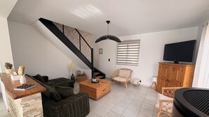 A living room with a sofa, coffee table, and a television on a wooden cabinet. - Charming house near the ocean and the village (Hillion)