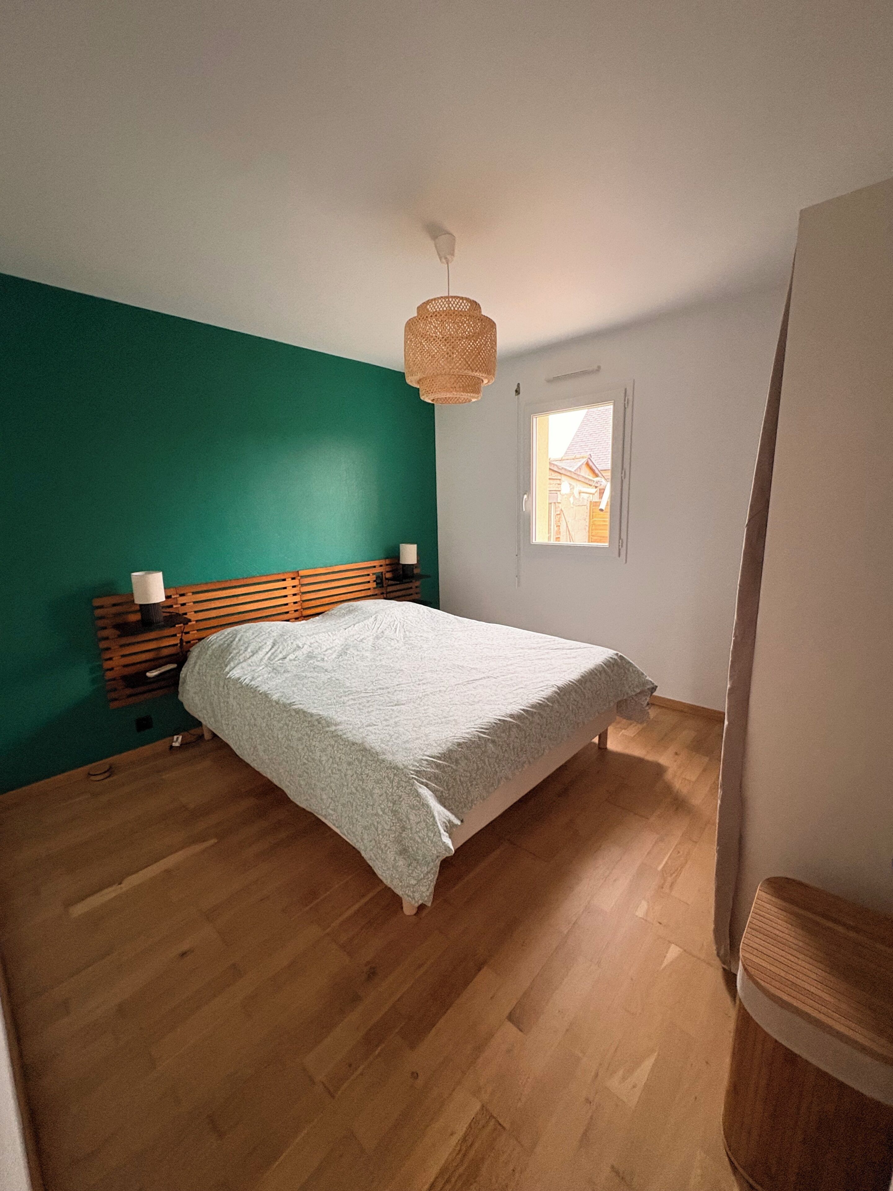 Een slaapkamer met een bed, nachtkastje, lamp, raam en deur.