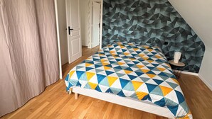 A bedroom with a sloped ceiling, a geometric-patterned bedspread, a wooden floor, and a door leading to another room. - Charming house near the ocean and the village (Hillion)