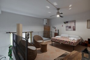 A bedroom with a bed, two wicker chairs, a small table, a ceiling fan, and a balcony with a railing. - Sanità inside By Dimorra  (Naples)