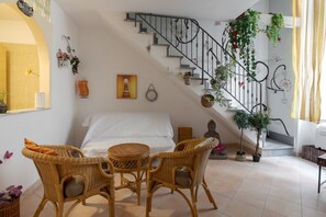 A bedroom with a bed, a small round table, wicker chairs, a staircase with a railing, and potted plants. - Sanità inside By Dimorra  (Naples)