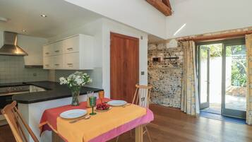 A dining area with a table set for two, a kitchen with white cabinets, and a stone wall.