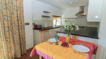 A modern kitchen with a dining area, featuring a table set for two with plates, cutlery, and a vase with flowers.