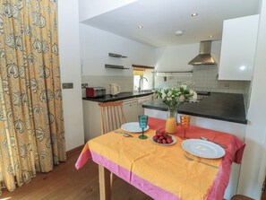 A modern kitchen with a dining area, featuring a table set for two with plates, cutlery, and a vase with flowers. - Frome Gazey Barn (Dorchester)
