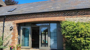 A brick building with a tiled roof, a glass door entrance, and a small garden area with potted plants.