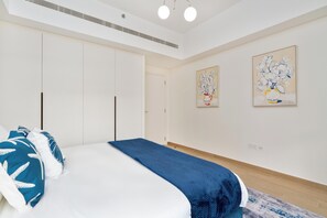 A bedroom with a bed, a wardrobe, and two wall-mounted paintings. - bnbme - Al Jazi - 2BR (Dubai)