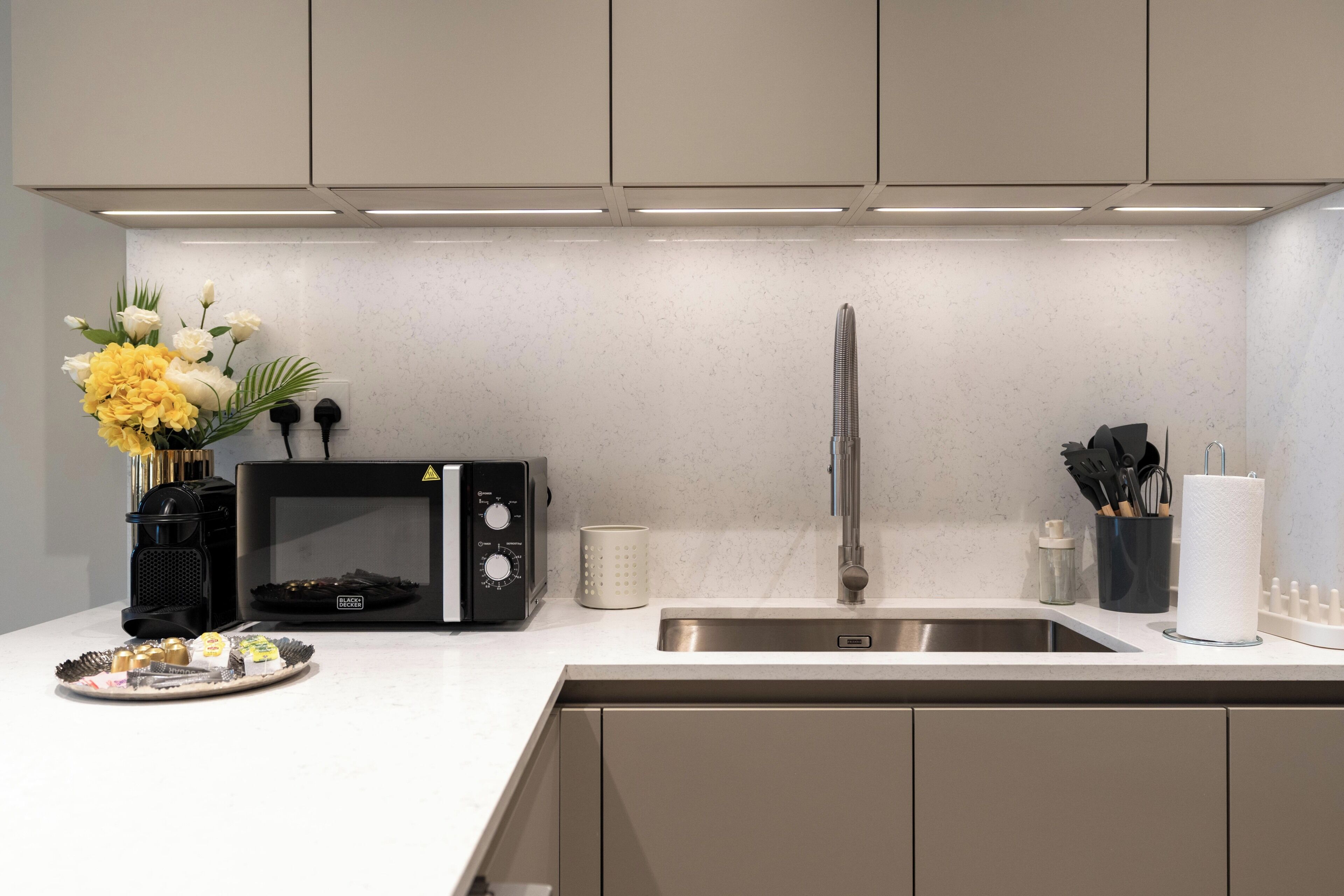 Una cocina moderna con microondas empotrado, pileta de acero inoxidable y un florero con flores en la encimera.