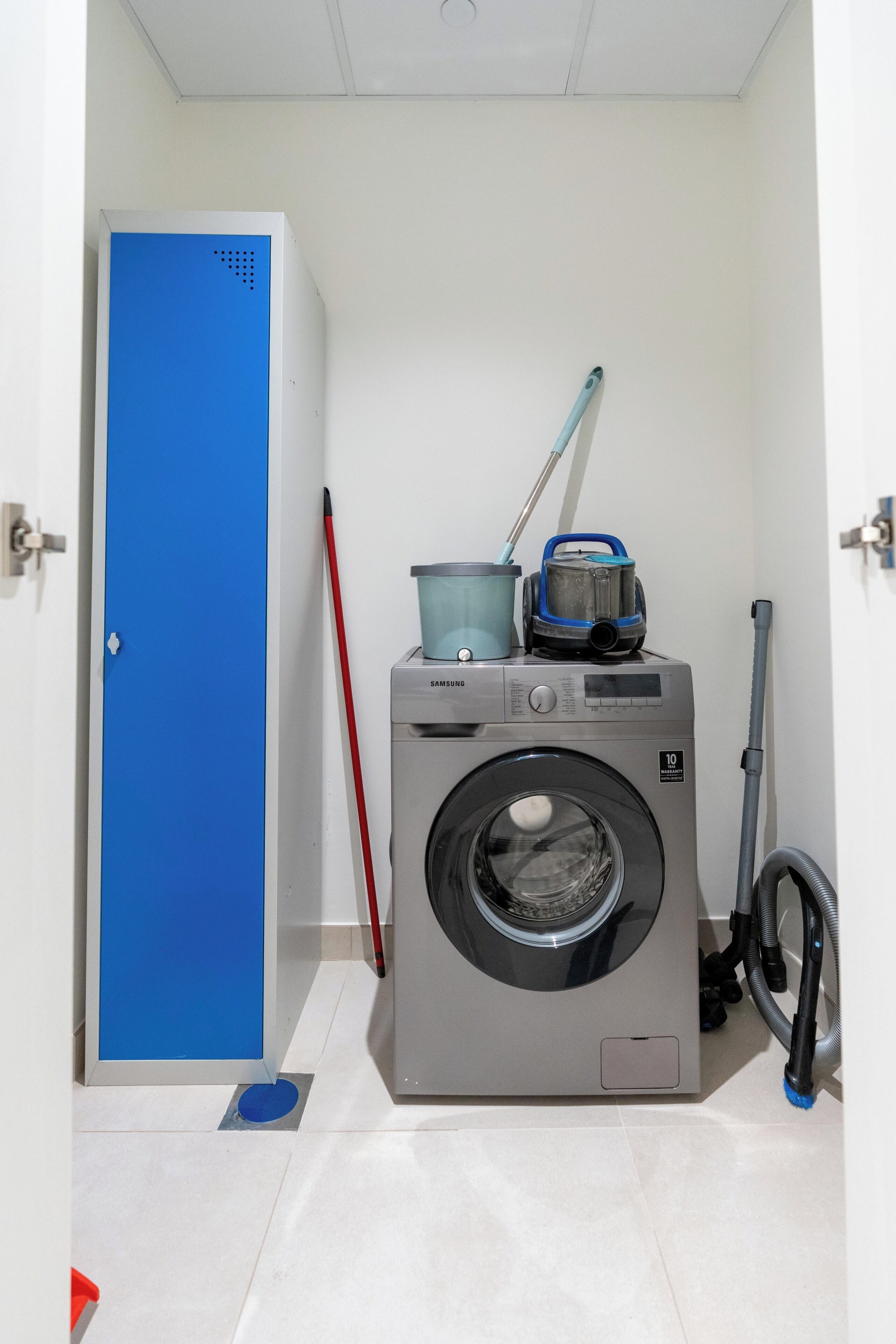 A compact laundry room with a washing machine, a mop, and a vacuum cleaner.