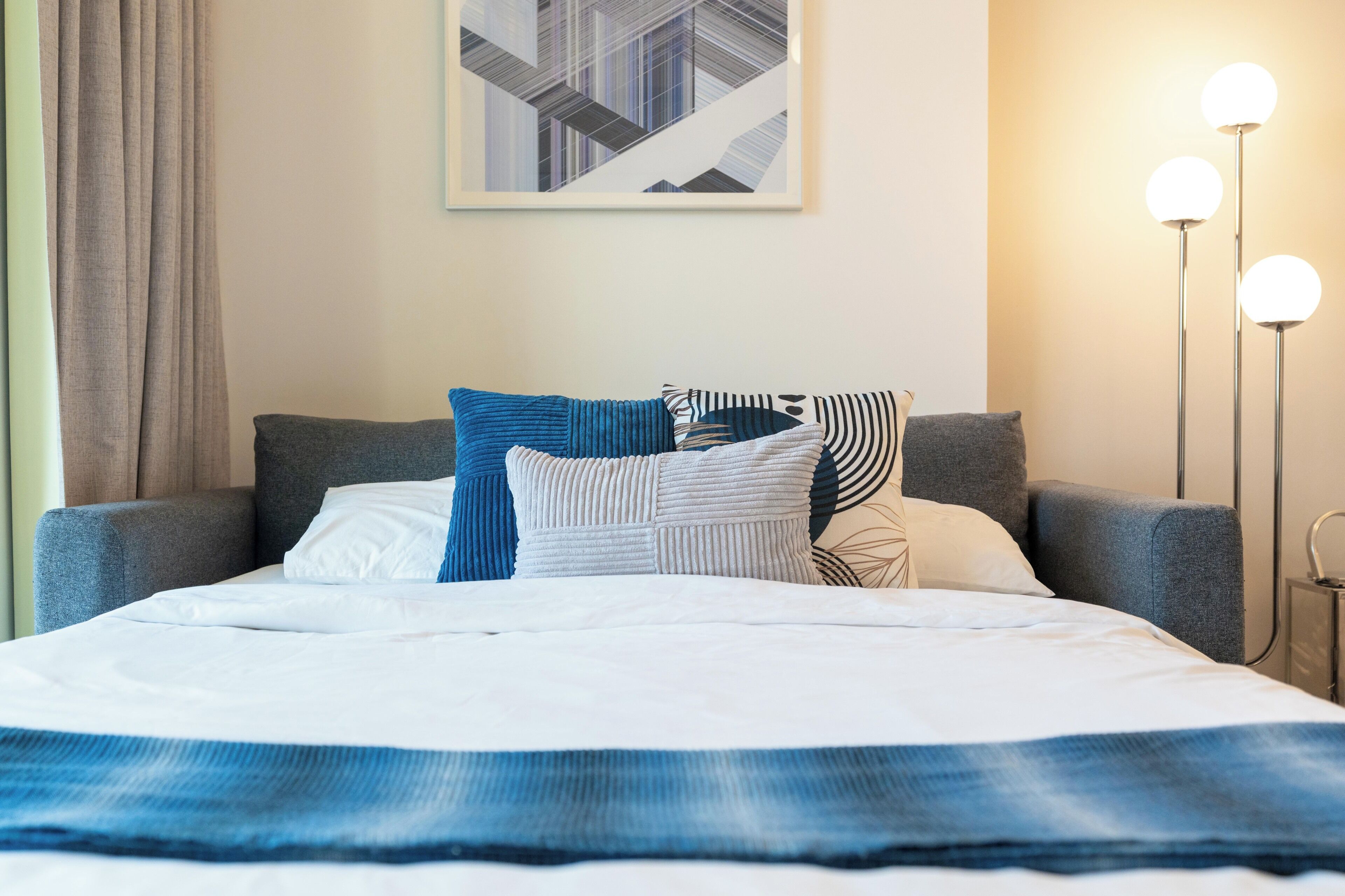 A neatly made bed with a blue and white striped blanket, a grey upholstered headboard, and a selection of pillows in various patterns and colors.