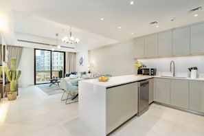 A modern kitchen with a central island, built-in appliances, and a dining area with a view. - bnbme - Al Jazi - 2BR (Dubai)