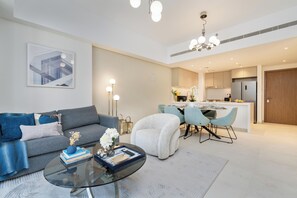 A modern living room with a sofa, a coffee table, and a dining area with chairs. - bnbme - Al Jazi - 2BR (Dubai)