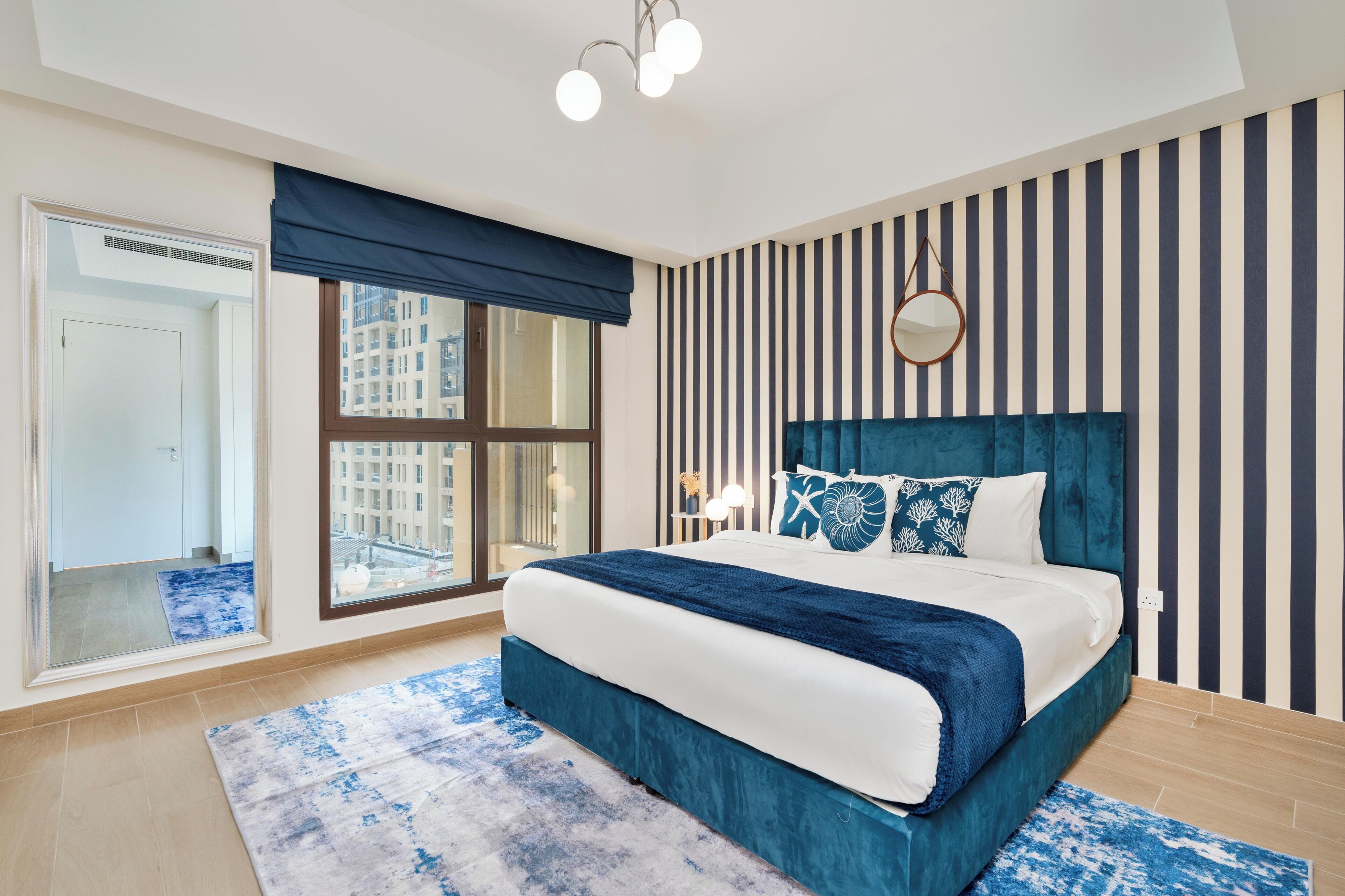 Un dormitorio moderno con una cama grande, papel tapiz a rayas y vista a edificios desde la ventana.