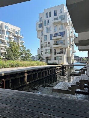 Un edificio residencial frente al agua, con balcones, un muelle y bancos de madera.