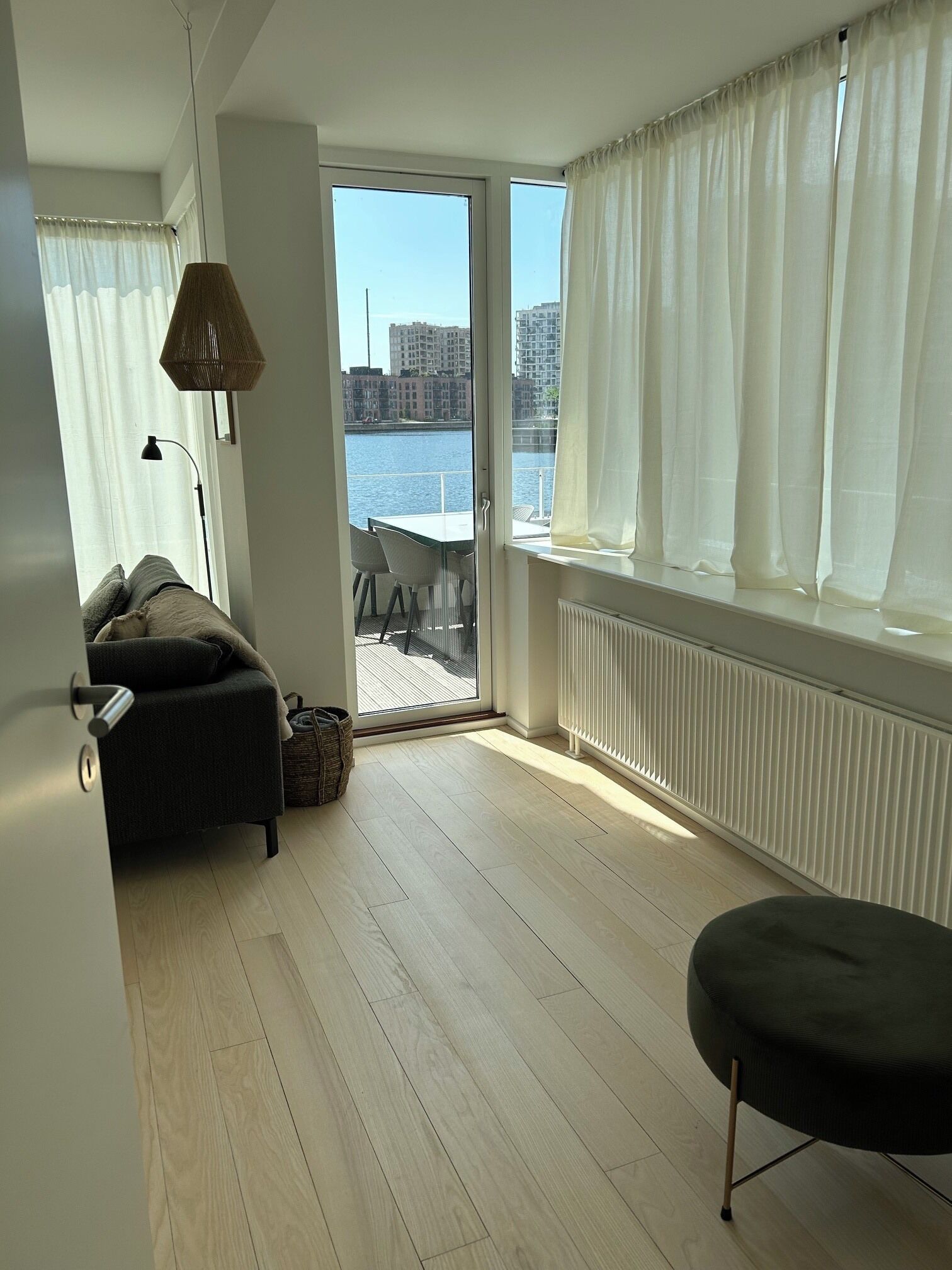 A room with a view of a body of water, a sofa, a table with chairs, and a lamp.