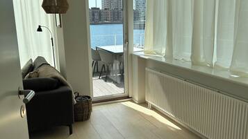 A room with a view of a body of water, a sofa, a table with chairs, and a lamp.