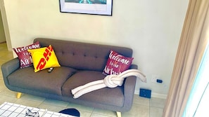 A grey sofa with two pillows, one with a red and white design and another with a red and yellow design, and a white rope tied around it.