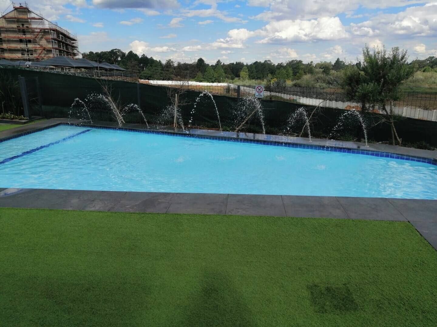 Una piscina con fuente, rodeada de césped y una cerca.