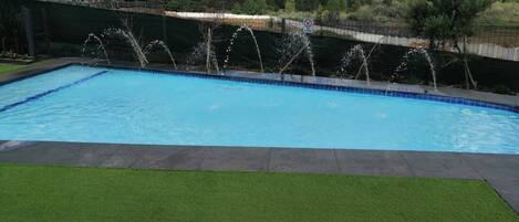 Una piscina con fuente, rodeada de césped y una cerca.