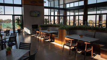 A spacious indoor area with multiple tables and chairs, large windows, and indoor plants.