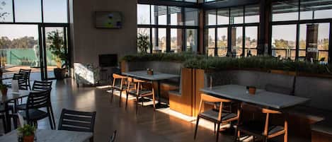 Een ruime binnenruimte met meerdere tafels en stoelen, grote ramen en kamerplanten.