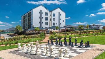 A large chessboard set up in a courtyard with a modern building in the background.