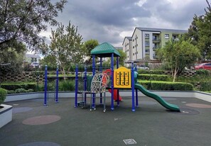 Un parque infantil con una estructura para escalar, un tobogán y una zona vallada.