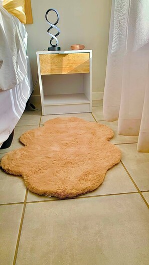 Un dormitorio con cama, mesita de noche, alfombra mullida y lámpara.