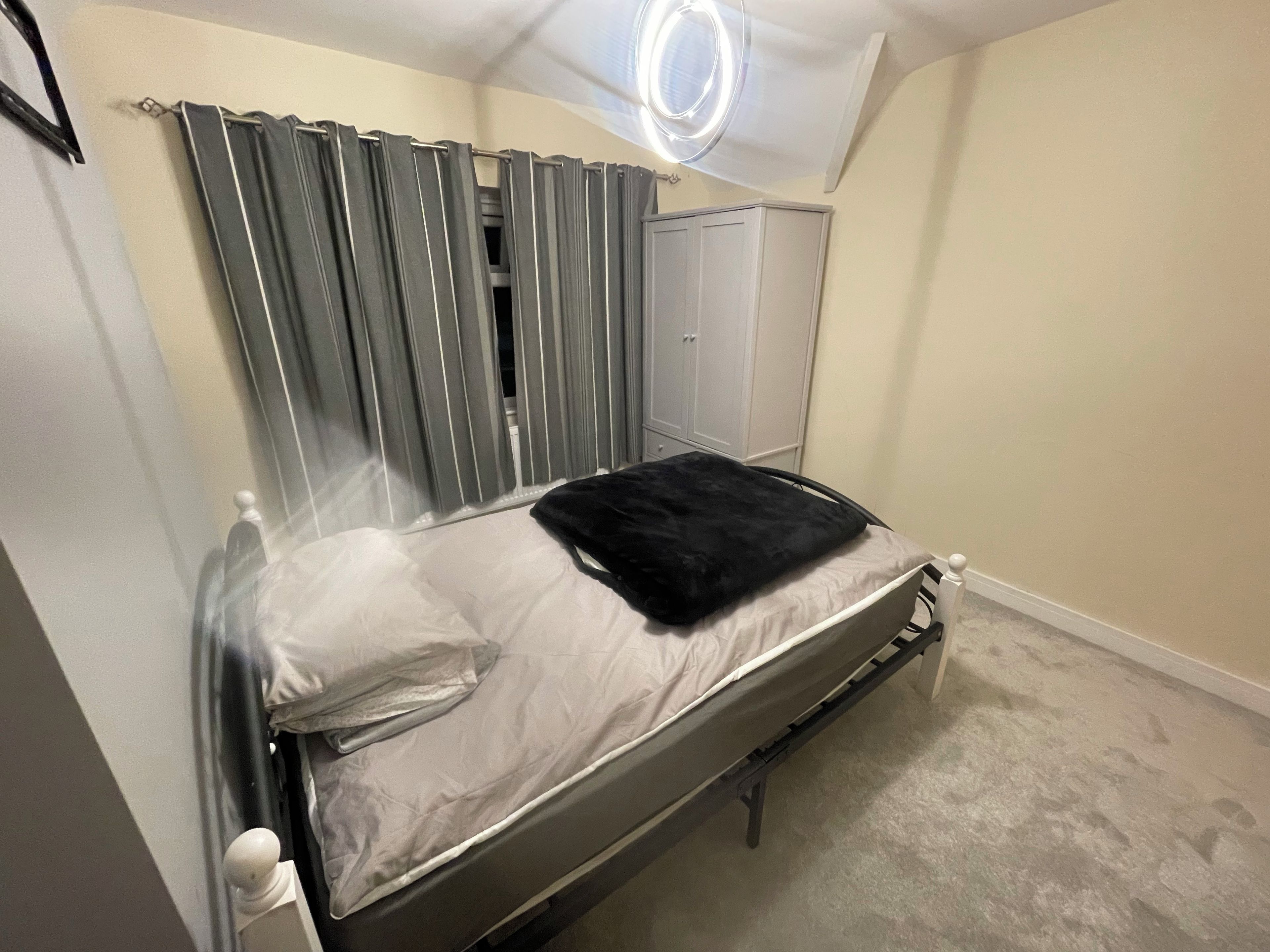 Une chambre à coucher avec un lit, des rideaux, une armoire et un luminaire au plafond.