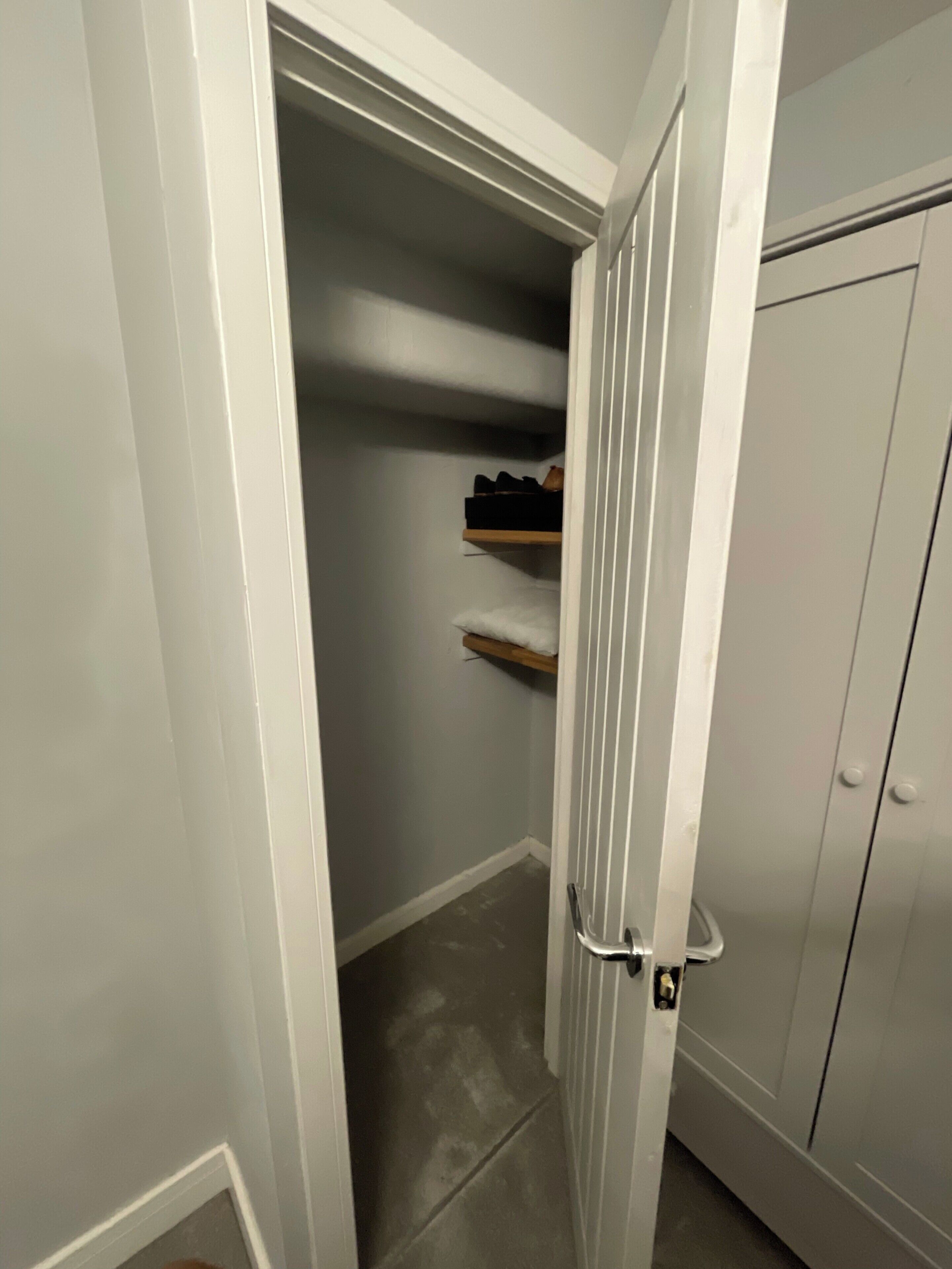 A narrow hallway with a door on the right, a closet with shelves, and a tiled floor.