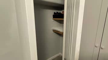 A narrow hallway with a door on the right, a closet with shelves, and a tiled floor.