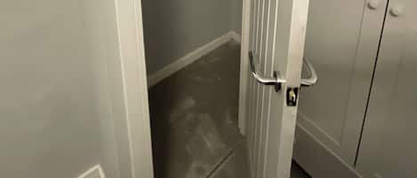 Un couloir étroit avec une porte sur la droite, un placard avec des étagères et un sol carrelé.