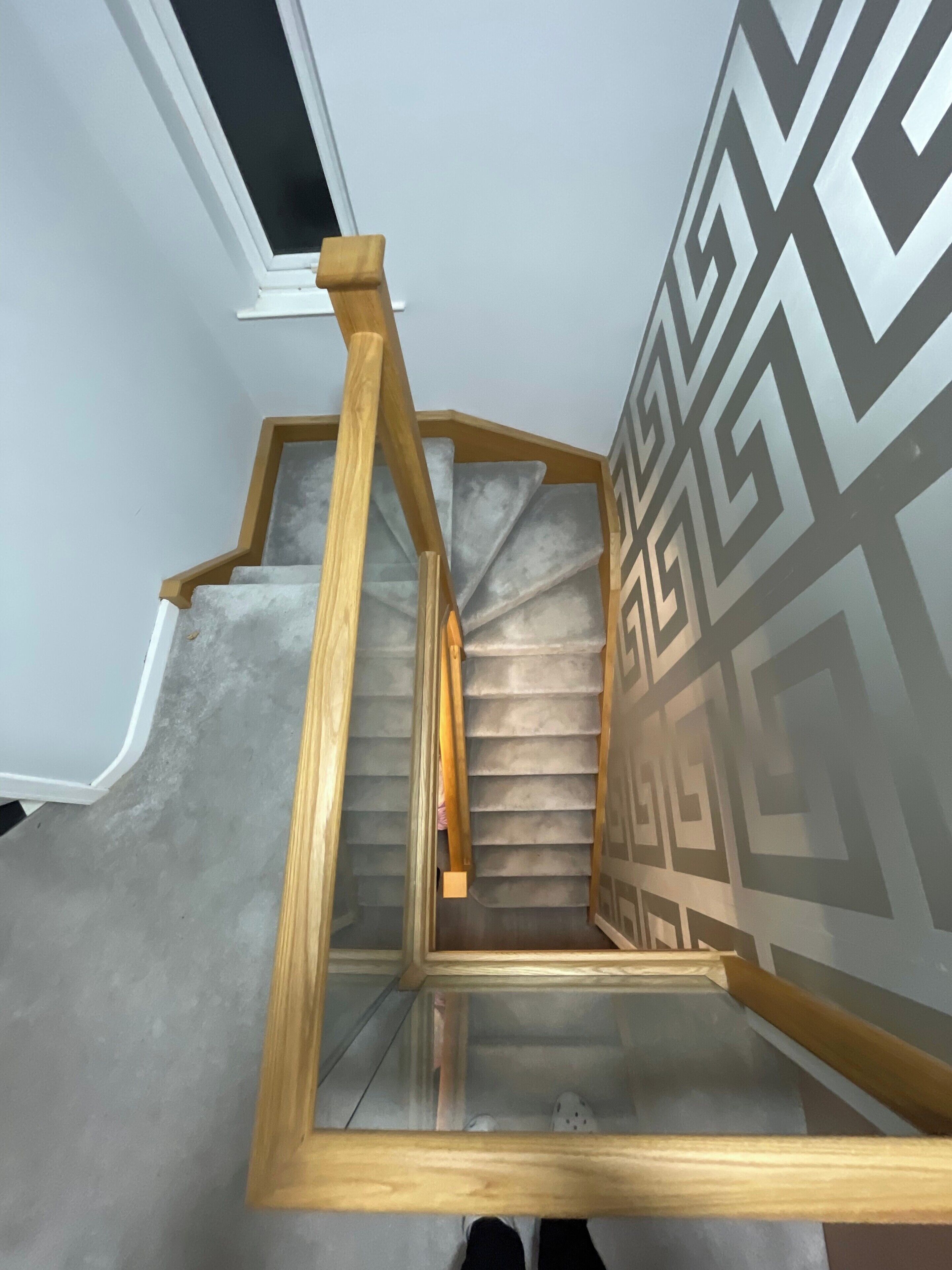 A staircase with wooden handrails and a glass balustrade, leading to a room with a patterned wall.