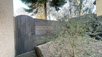 Een houten hek met horizontale latten, een grindpad en een kleine boom.