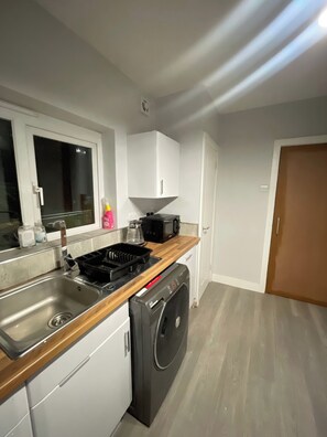 A compact kitchen with a sink, stove, microwave, and a washing machine. - Cozy Retreat in Stoke-on-trent (Stoke-on-Trent)
