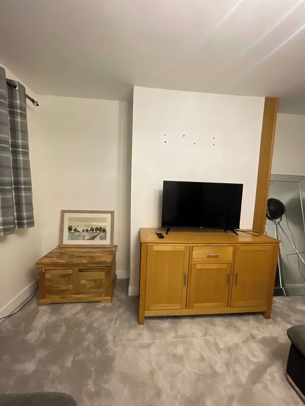 A room with a wooden cabinet, a flat-screen TV on top, a framed picture on the cabinet, and a lamp on a stand.