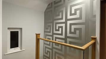 Een trap met een wand met een geometrisch patroon, een klein raam en een plafondlamp.