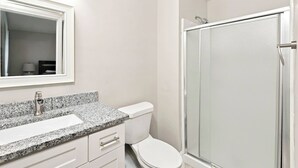 Ein Badezimmer mit einer Granit-Arbeitsplatte, einer weißen Toilette und einer Duschkabine aus Glas.