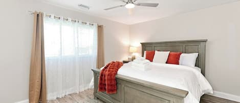Un dormitorio con cama, ventilador de techo, mesita de noche y ventana con cortinas.