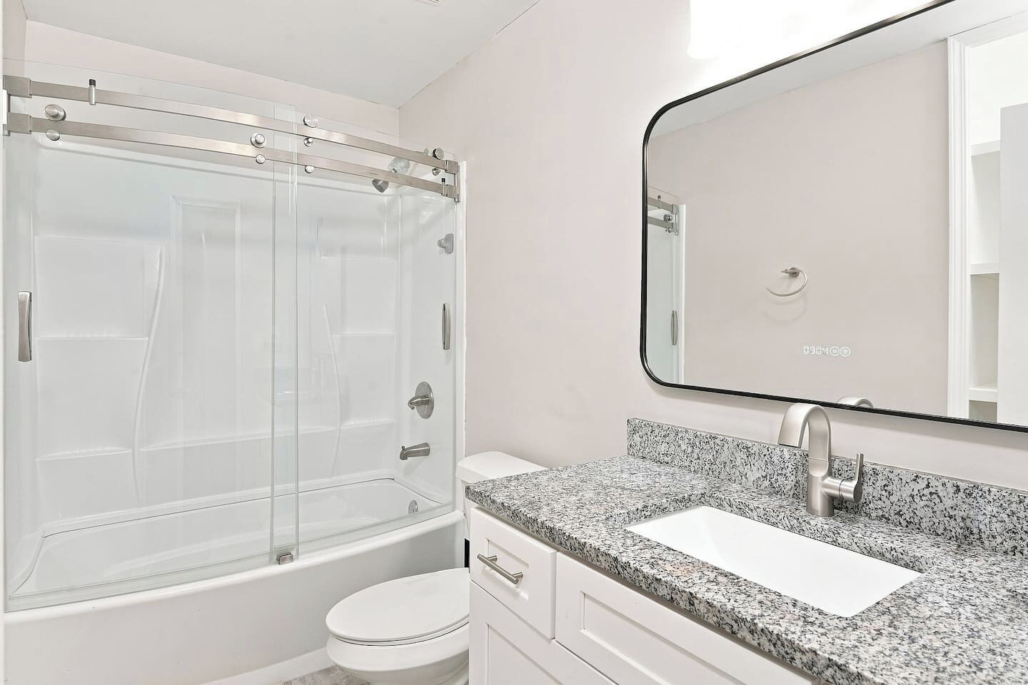 A modern bathroom with a glass-enclosed shower, a white toilet, a granite countertop sink, and a large mirror.