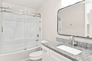 A modern bathroom with a glass-enclosed shower, a white toilet, a granite countertop sink, and a large mirror. - Peachwood Hideaway at Briarcliff (Atlanta)