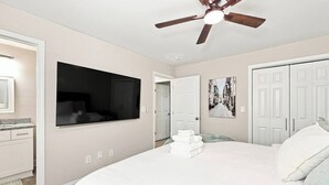 Ein Schlafzimmer mit einem großen Bett, einem Deckenventilator, einem Flachbildfernseher, einer Tür und einem an der Wand hängenden Bild.