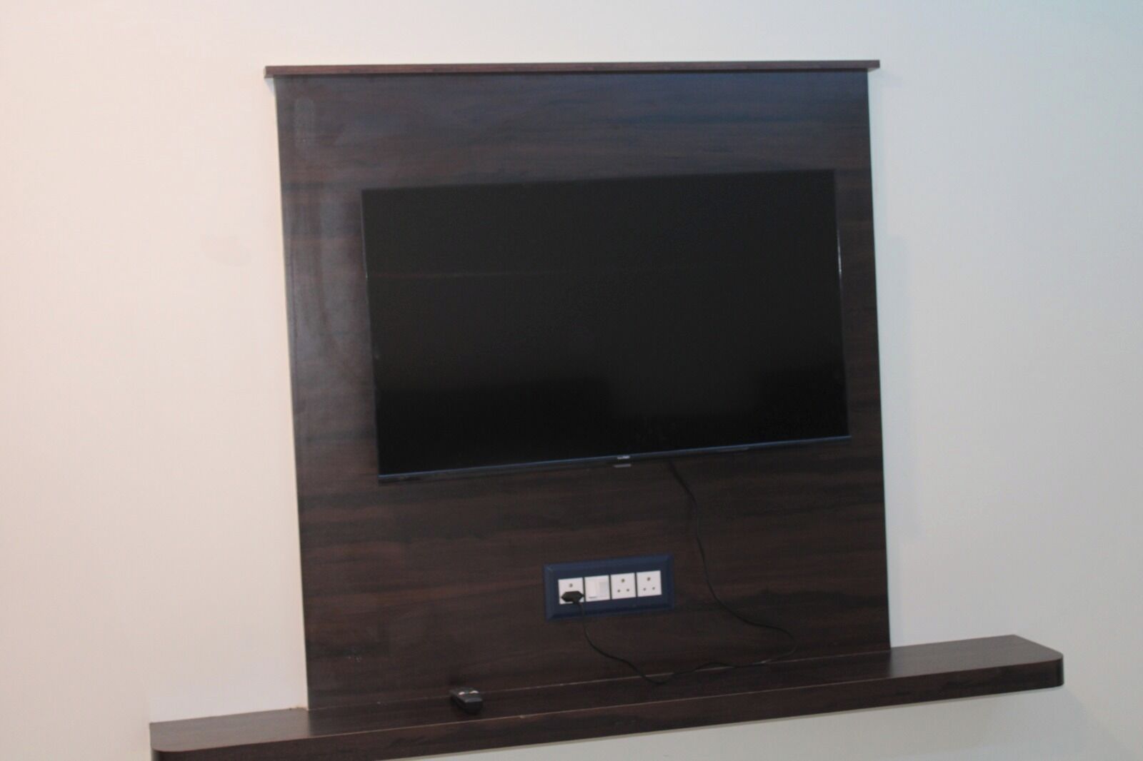 A flat-screen TV mounted on a dark wooden wall with a power outlet below it.