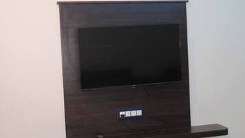 A flat-screen TV mounted on a dark wooden wall with a power outlet below it.
